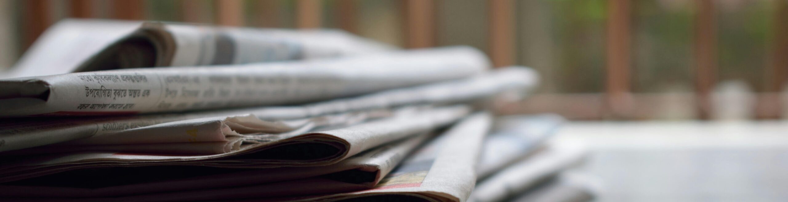 A close-up of a stack of newspapers resting on a desk, symbolizing information and media.